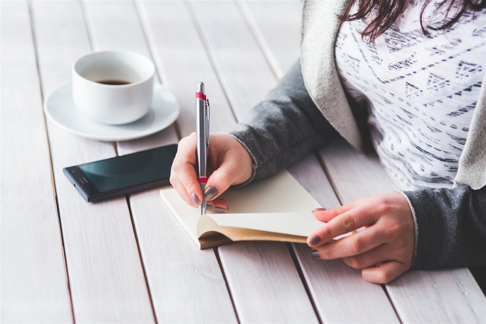 Person writing notes beside a phone and coffee during a focused work session